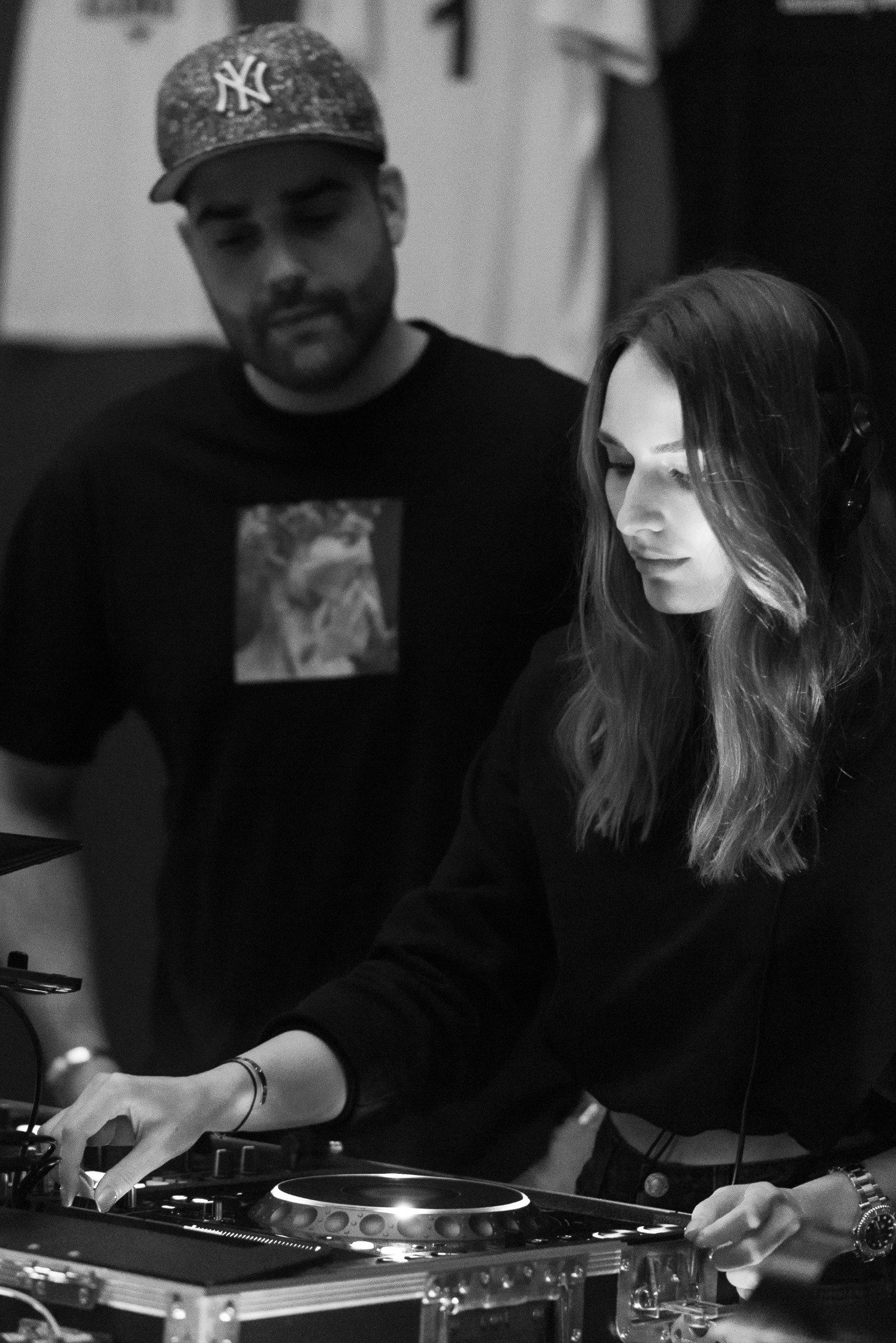 Black-and-white documentary portrait of a female DJ at the console with a man behind her