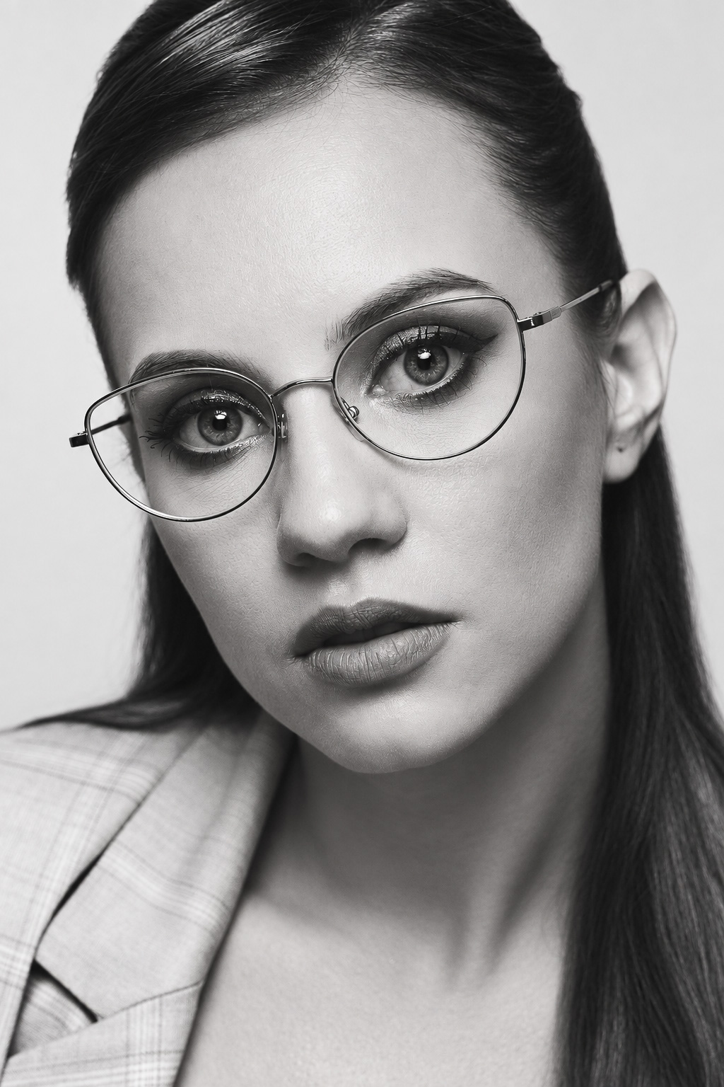 Black-and-white close portrait of a woman wearing glasses and a checked jacket