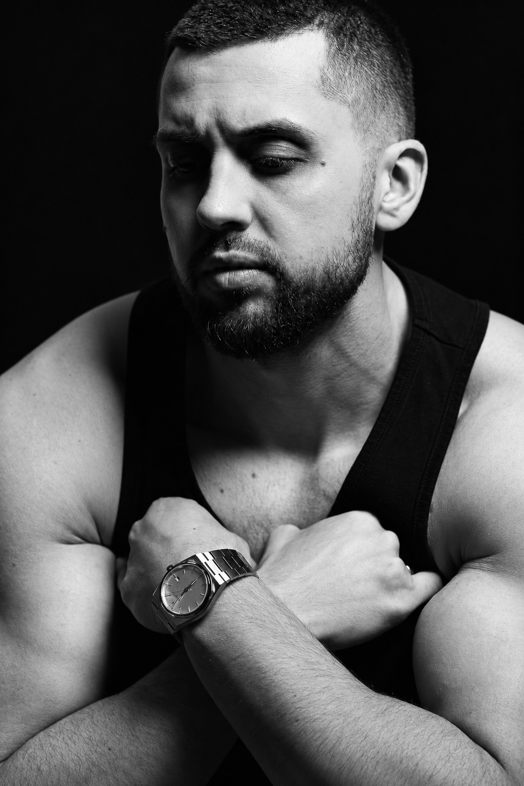 Black-and-white portrait of a man in a dark vest with crossed arms and a wristwatch