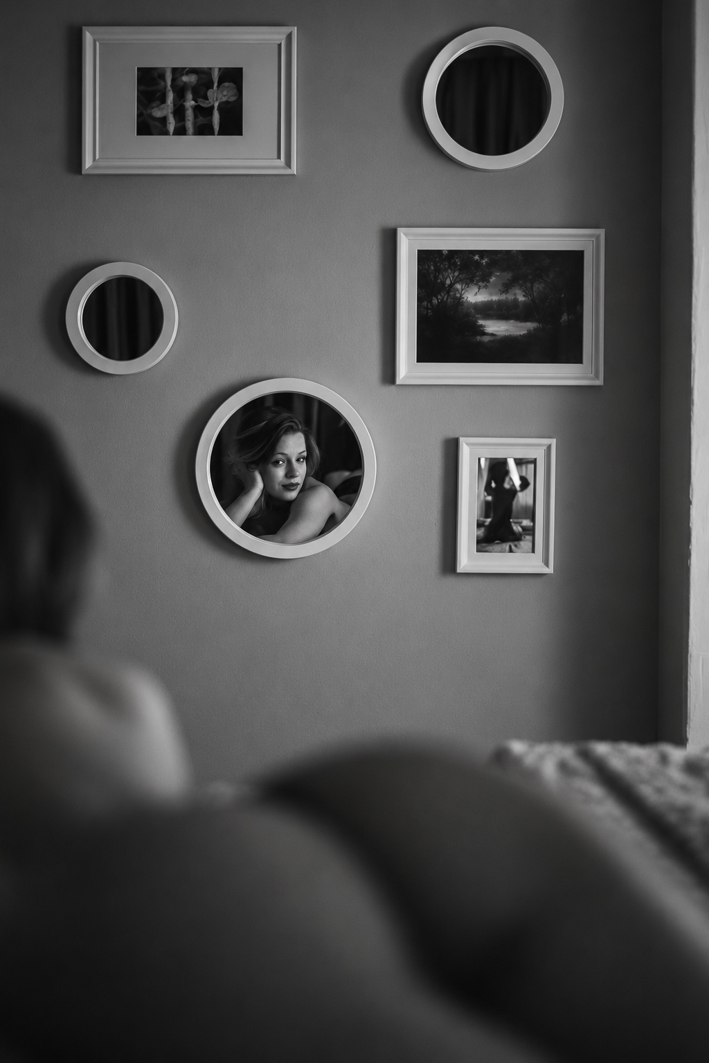 Black-and-white portrait of a woman reflected in a round mirror among framed pictures